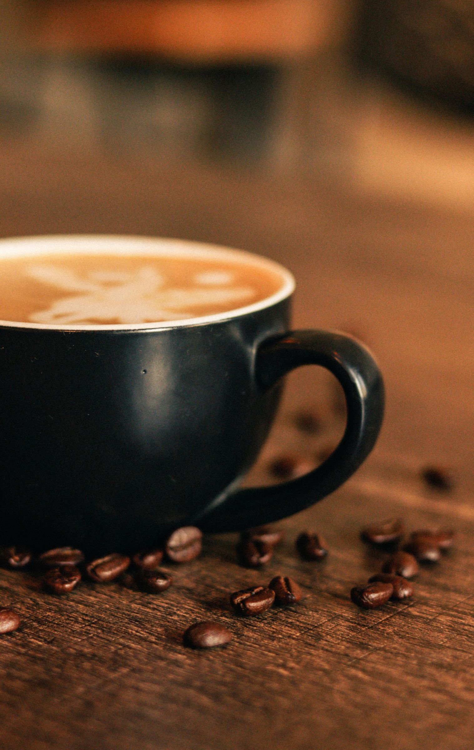 Un latte art dans une tasse noire, entouré de grains de café.
